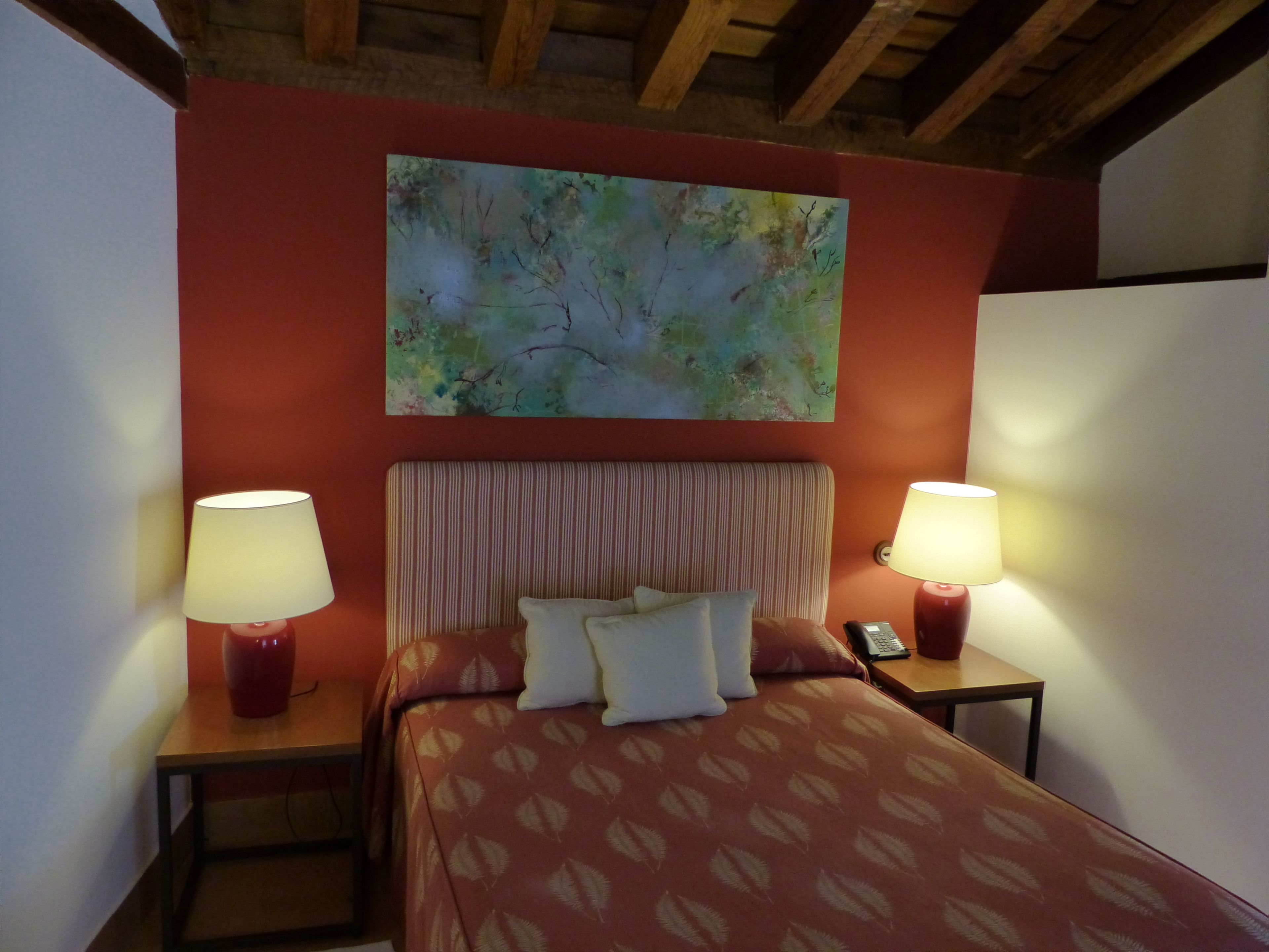 A hotel room with a bed, two bedside tables with lamps, a telephone, and a painting on the wall.