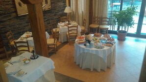 Un comedor con mesas redondas cubiertas con manteles blancos, sillas de madera y una variedad de alimentos.