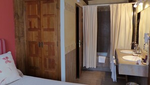 Un dormitorio con puerta de madera, cama con almohada blanca y baño con lavamanos y espejo.