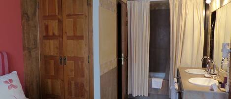 Une chambre avec une porte en bois, un lit avec un oreiller blanc et une salle de bain avec un lavabo et un miroir.