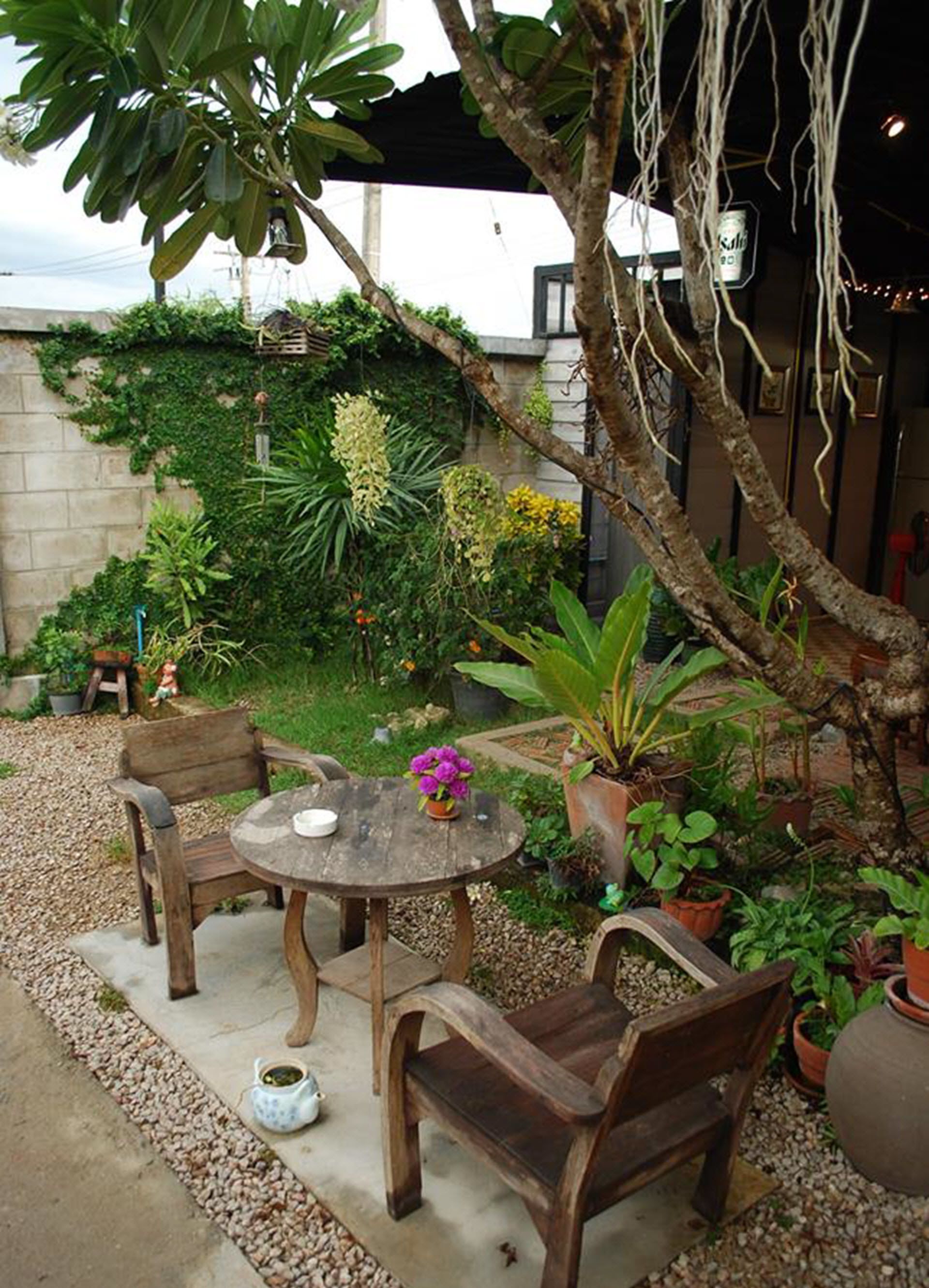 A patio with a round wooden table and chairs, surrounded by potted plants and a small garden area.