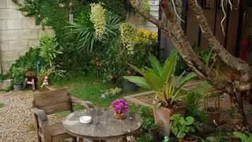 A patio with a round wooden table and chairs, surrounded by potted plants and a small garden area.