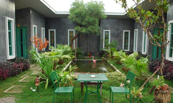 Un patio con un pequeño estanque, sillas verdes y una mesa.
