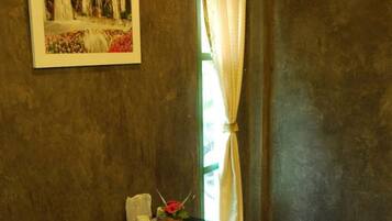 A small room with a glass table, two wooden stools, a framed painting of a waterfall, and a window with curtains.