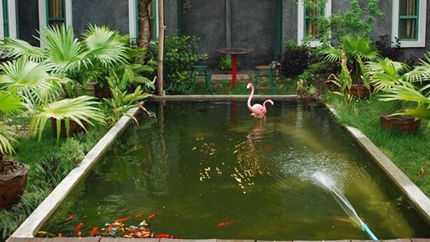A courtyard with a pond, a flamingo, and various plants. - Chatchanan Resort (Mae Sot)