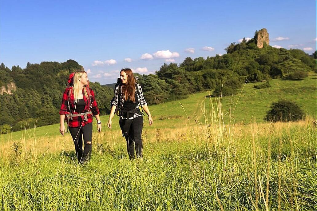 Two people walking in a grassy field with a forested hill in the background.