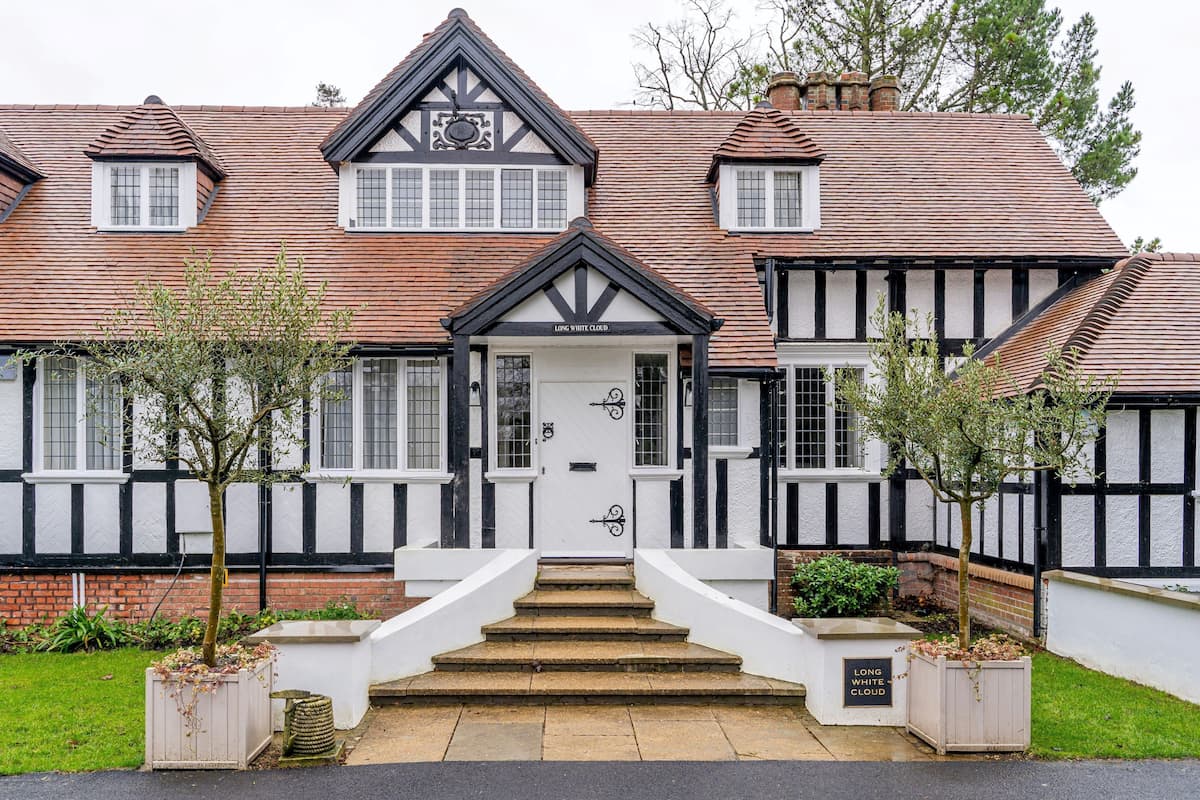 Ein traditionelles Haus im Tudor-Stil mit steiler Dachneigung, weißer und schwarzer Fachwerkkonstruktion und einer symmetrischen Fassade.