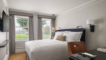 A hotel room with a large bed, a desk, a chair, a TV mounted on the wall, and a window with curtains.