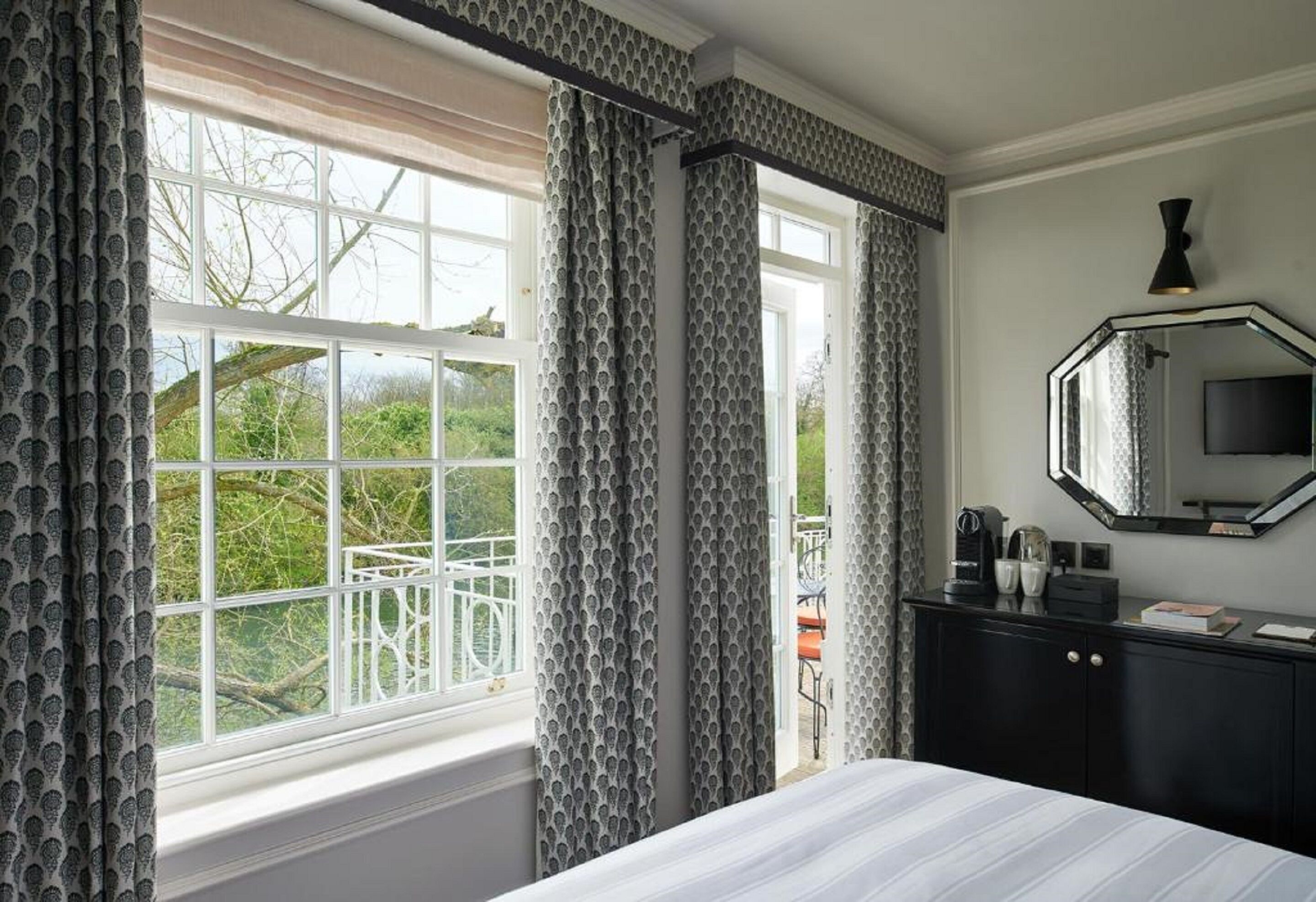 Une chambre avec une grande fenêtre, un lit, une commode, un miroir et une machine à café.