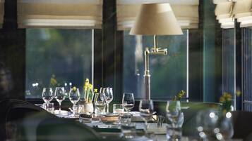 A dining table set with multiple wine glasses and a vase with flowers, with a lamp and hanging light fixture above.