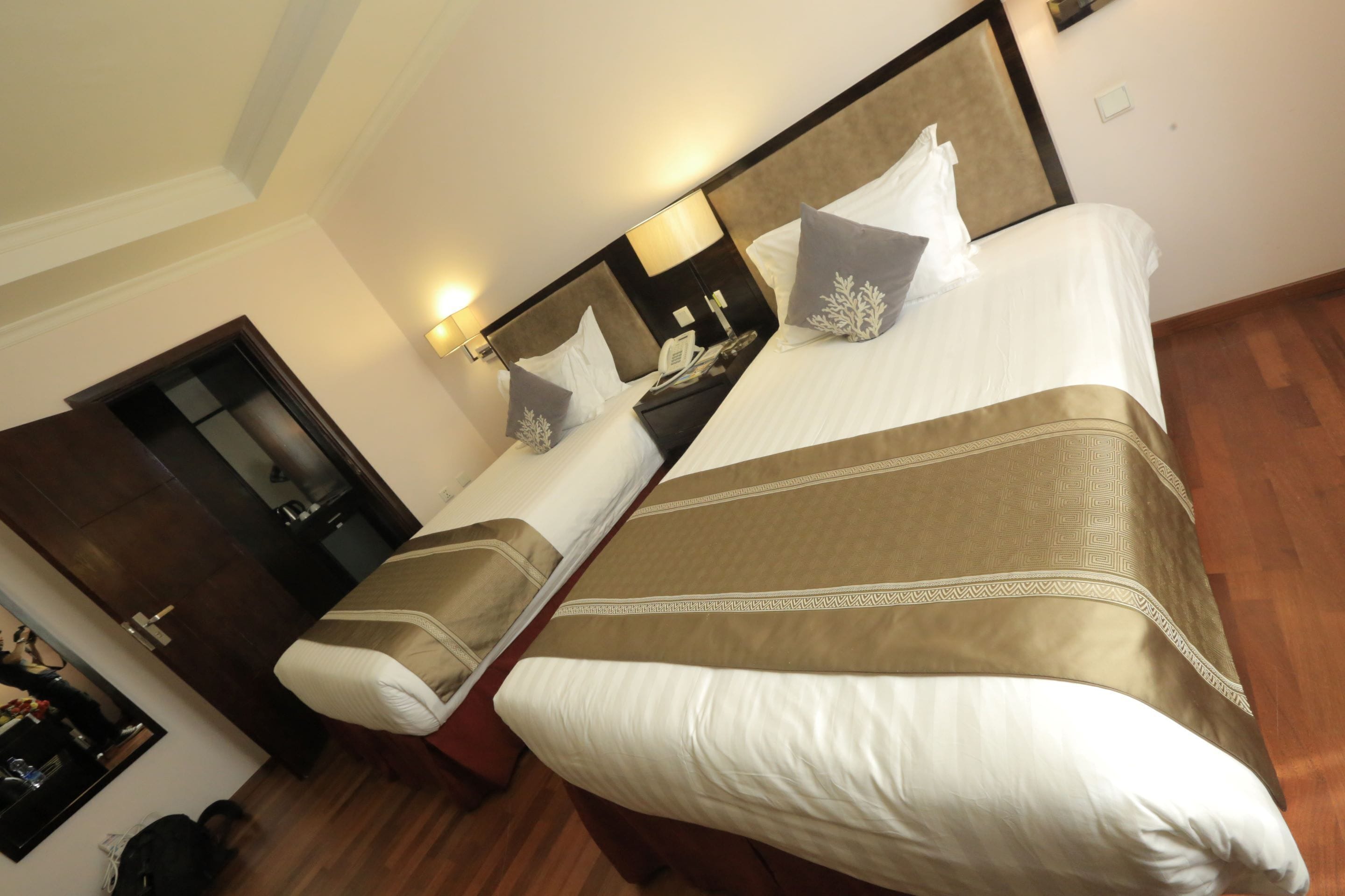 A hotel room with a large bed, a bedside table, a nightstand, a mirror, and a wooden floor.