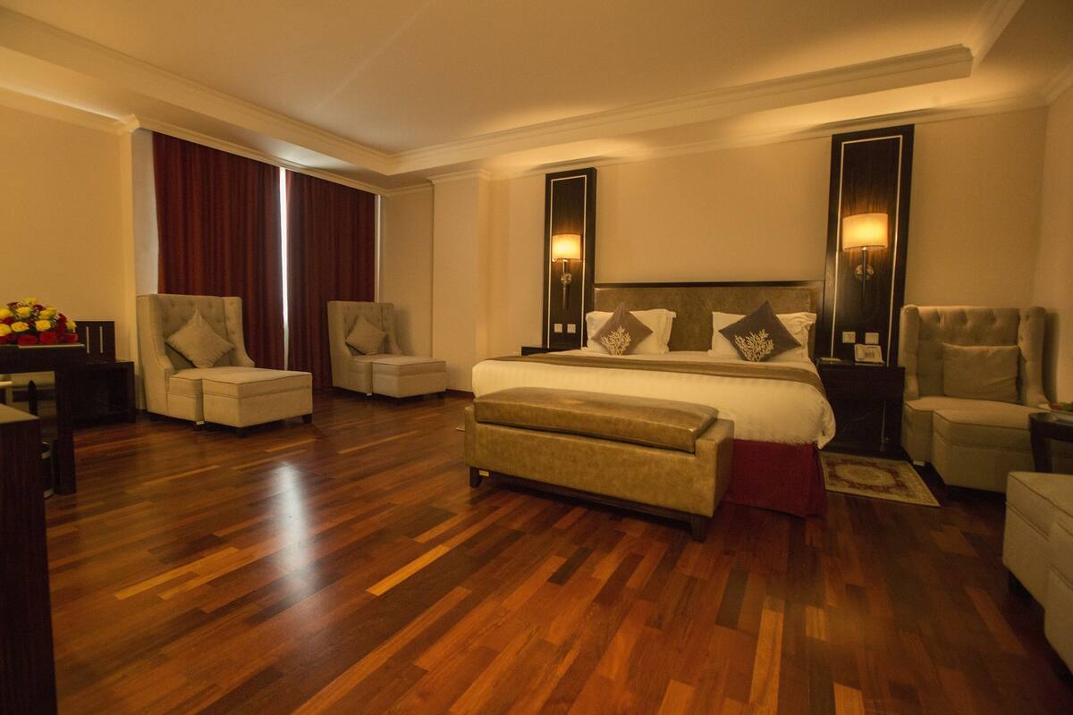 A spacious hotel room with a large bed, two armchairs, a sofa, and a wooden floor.