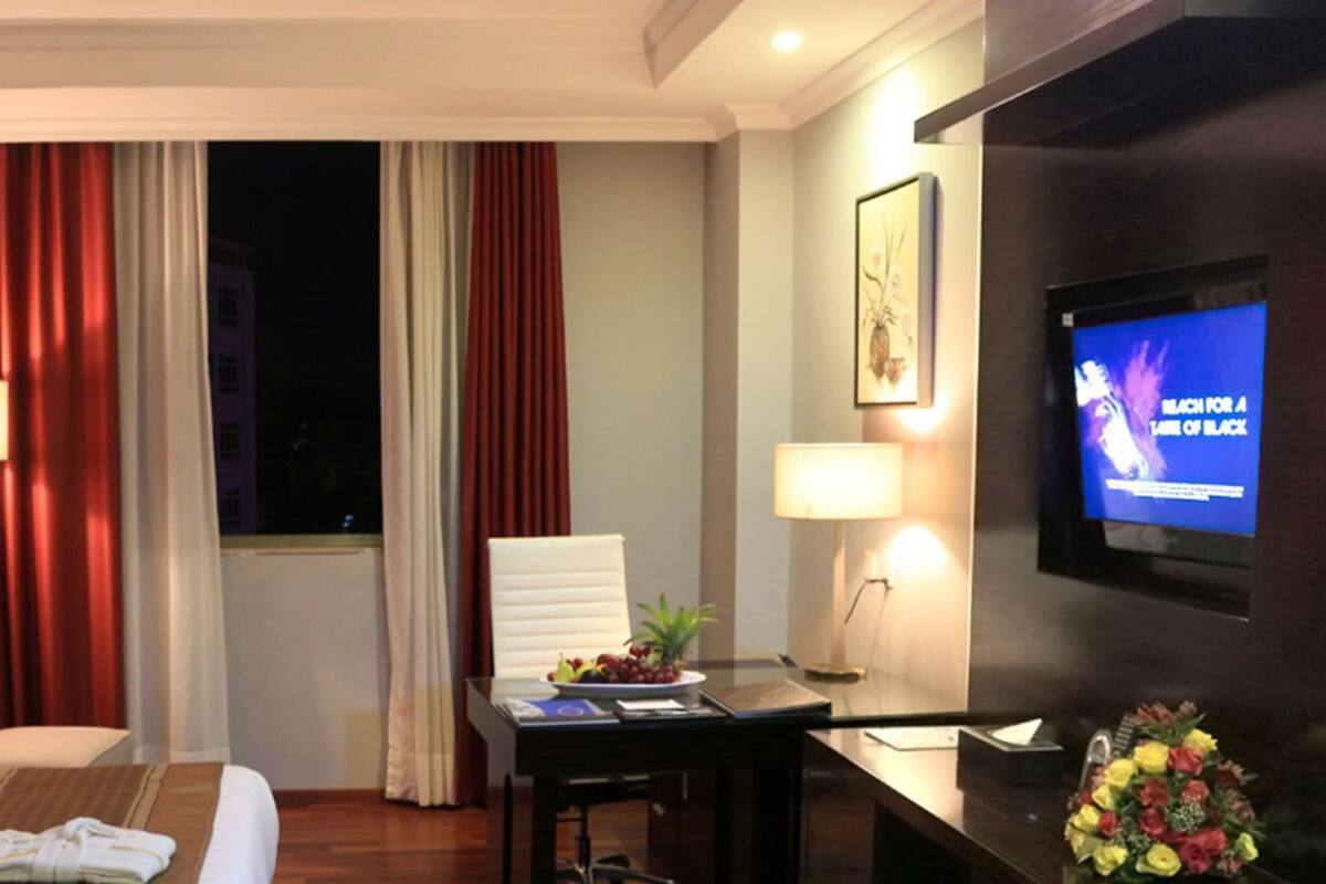 A hotel room with a bed, a desk, a chair, a TV, and a window with curtains.