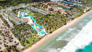 Vista aérea de un resort con varias edificaciones, una piscina serpenteante y acceso a la playa.