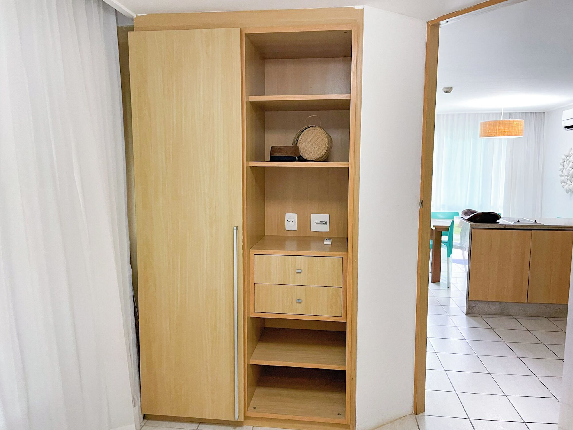 Un armario de madera con varios estantes y cajones, un cesto para colgar y enchufes eléctricos.