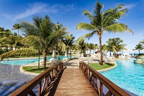 A wooden deck leading to a pool surrounded by palm trees and lounge chairs. - Beach Class Muro Alto BY AFT (Ipojuca)