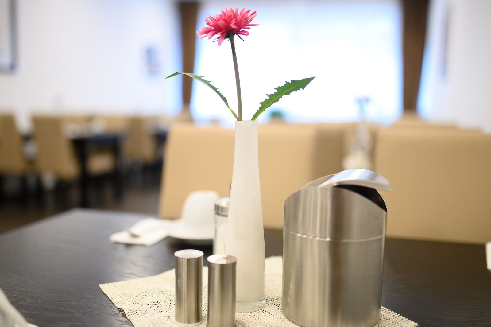 A table with a vase containing a pink flower, two salt shakers, and a metal pitcher.
