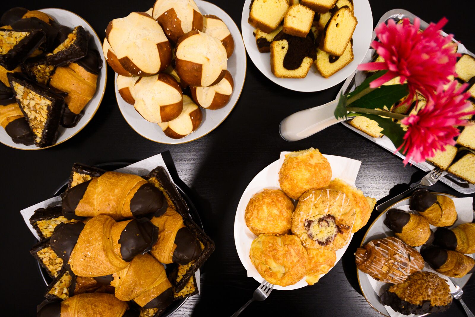 A variety of pastries and desserts on plates, with a vase of flowers in the background.