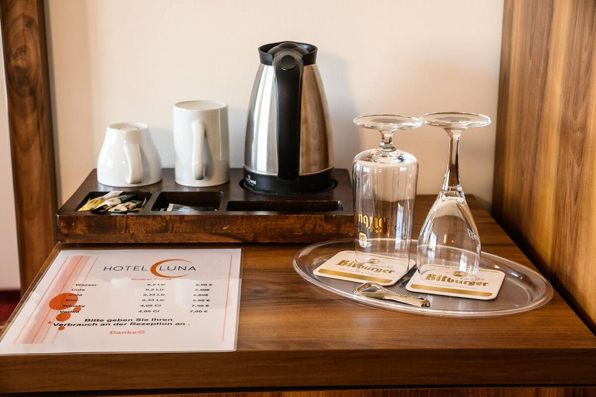 Un mini-bar d’hôtel comprenant une carte des boissons, une machine à café, des verres et un plateau avec une bouteille et des verres.