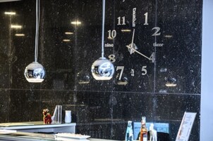 Un reloj de pared sobre un fondo de mármol negro, con el reflejo de una persona.