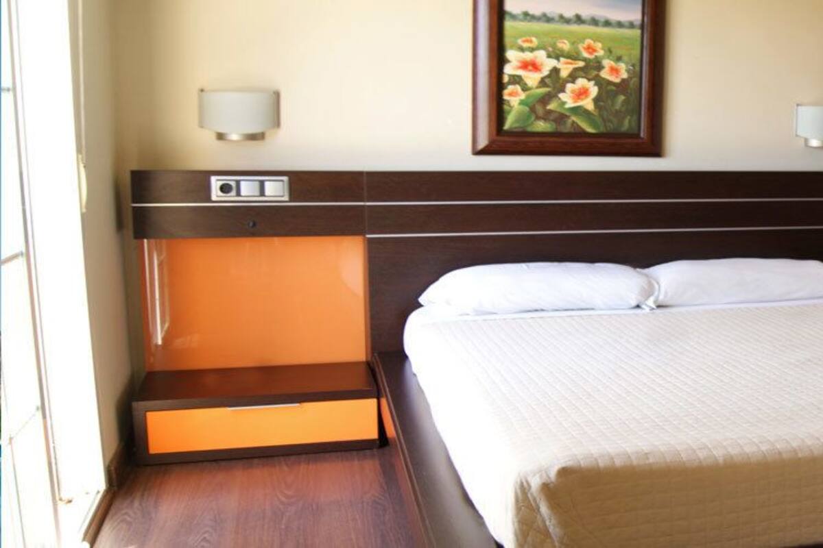 A hotel room with a large bed, two bedside tables, a nightstand, a painting on the wall, and two wall-mounted lamps.