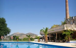 A swimming pool with lifebuoys, palm trees, and a building with a balcony overlooking the pool. - Hotel Las Navas (Malagon)