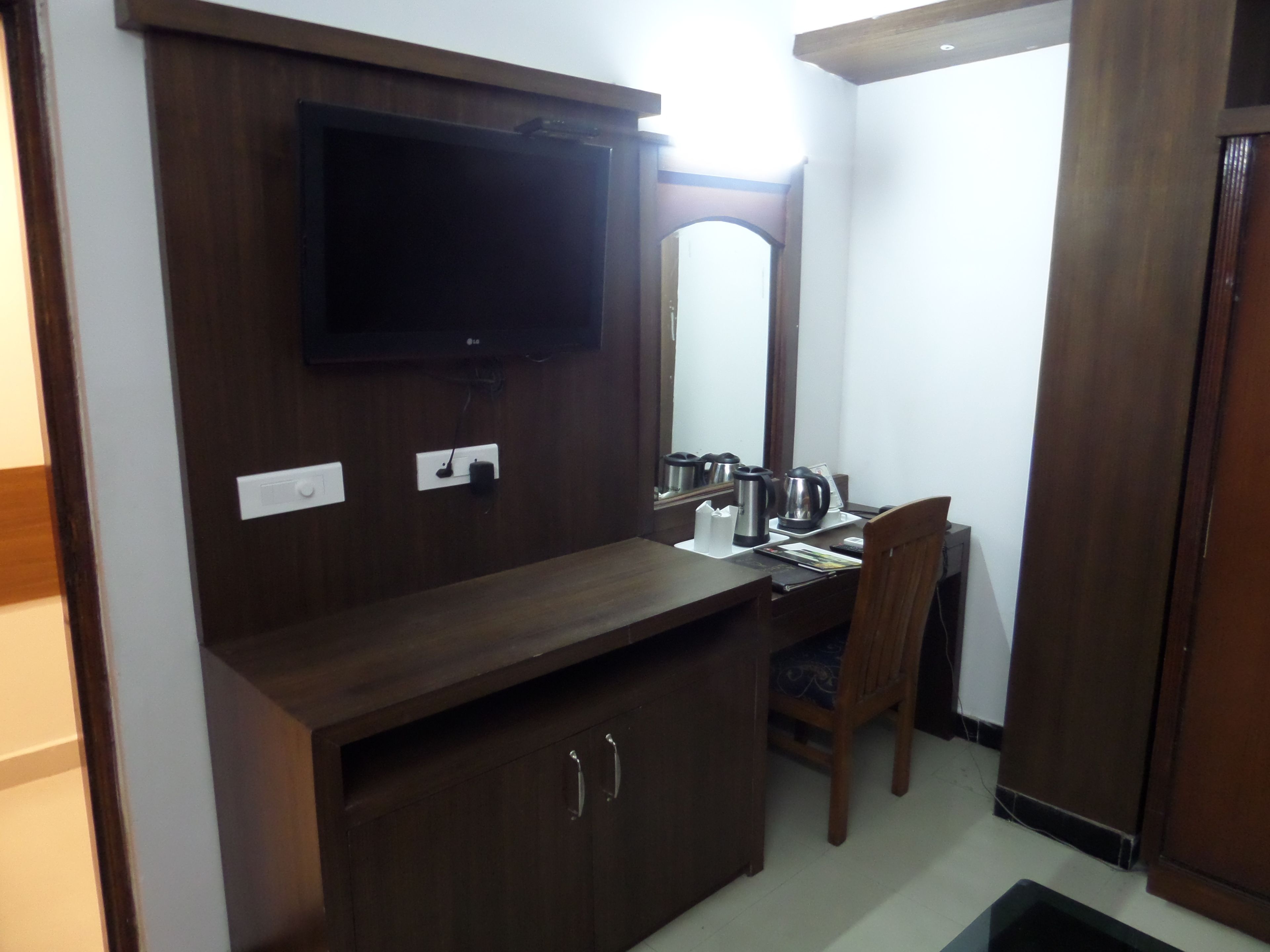 Habitación de hotel con un escritorio de madera, un televisor montado en la pared, un espejo y un armario con cajones.