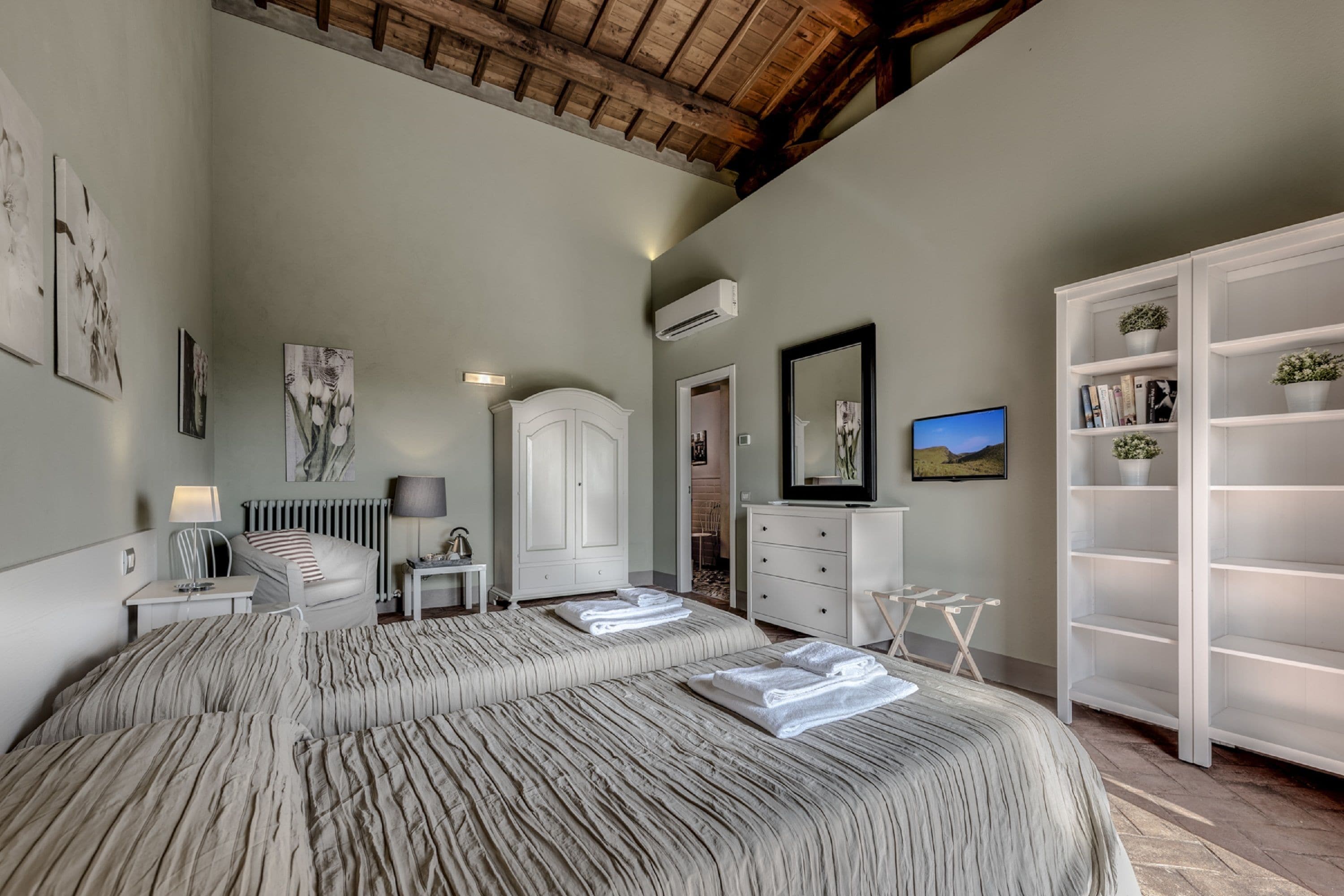 A bedroom with a large bed, a wardrobe, a mirror, and a television.