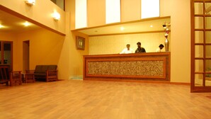 A reception area with a wooden reception desk, two staff members, and a patterned wall. - Raahat Inn Kodaikanal (Kodaikanal)