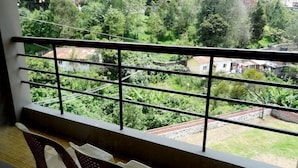 A balcony with a metal railing, a view of a lush green garden, and a glimpse of houses in the background. - Raahat Inn Kodaikanal (Kodaikanal)