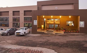 A building with a modern entrance, two parked cars, and a sign indicating a hotel.