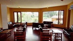 A spacious room with large windows, wooden furniture, and a view of greenery outside. - Raahat Inn Kodaikanal (Kodaikanal)