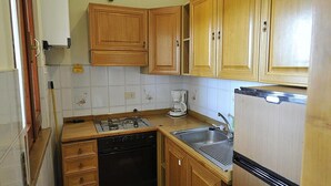 A compact kitchen with wooden cabinets, a dishwasher, a stove, and a refrigerator.