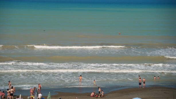 Una playa con gente nadando y de pie en el agua.