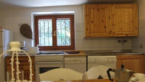 Una cocina con armarios de madera, estufa, lavavajillas y ventana con vista a la vegetación.