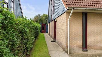 Een smalle pad tussen twee bakstenen huizen, met een kleine tuin en een rode deur.