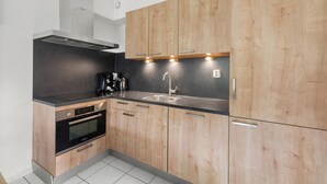 Una cocina moderna con armarios de madera, encimera negra, pileta de acero inoxidable y horno empotrado.