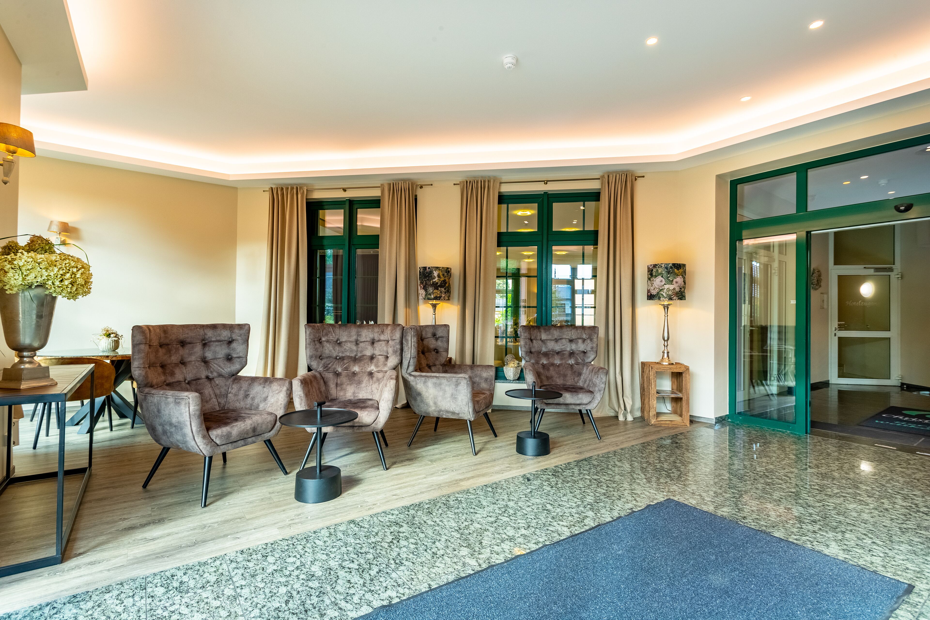 A modern hotel lobby with three plush armchairs, a dining table, and a large vase of flowers.