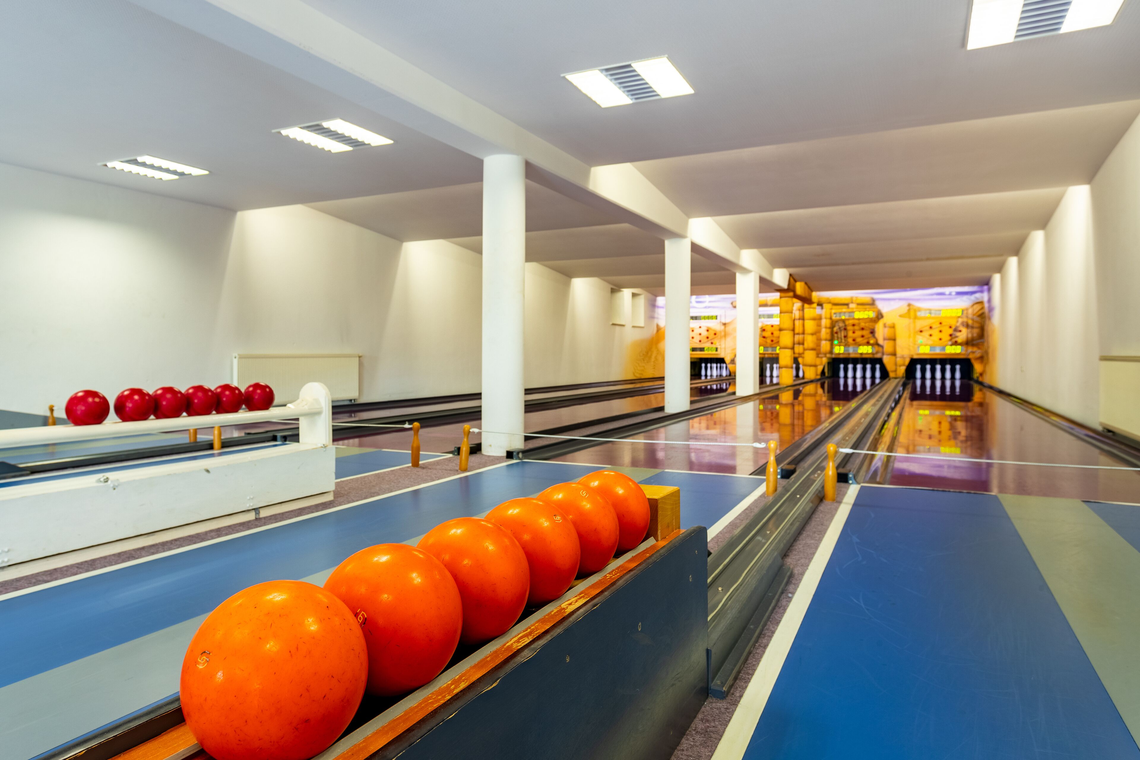 A bowling alley with multiple lanes, a bowling ball rack, and a seating area with chairs.