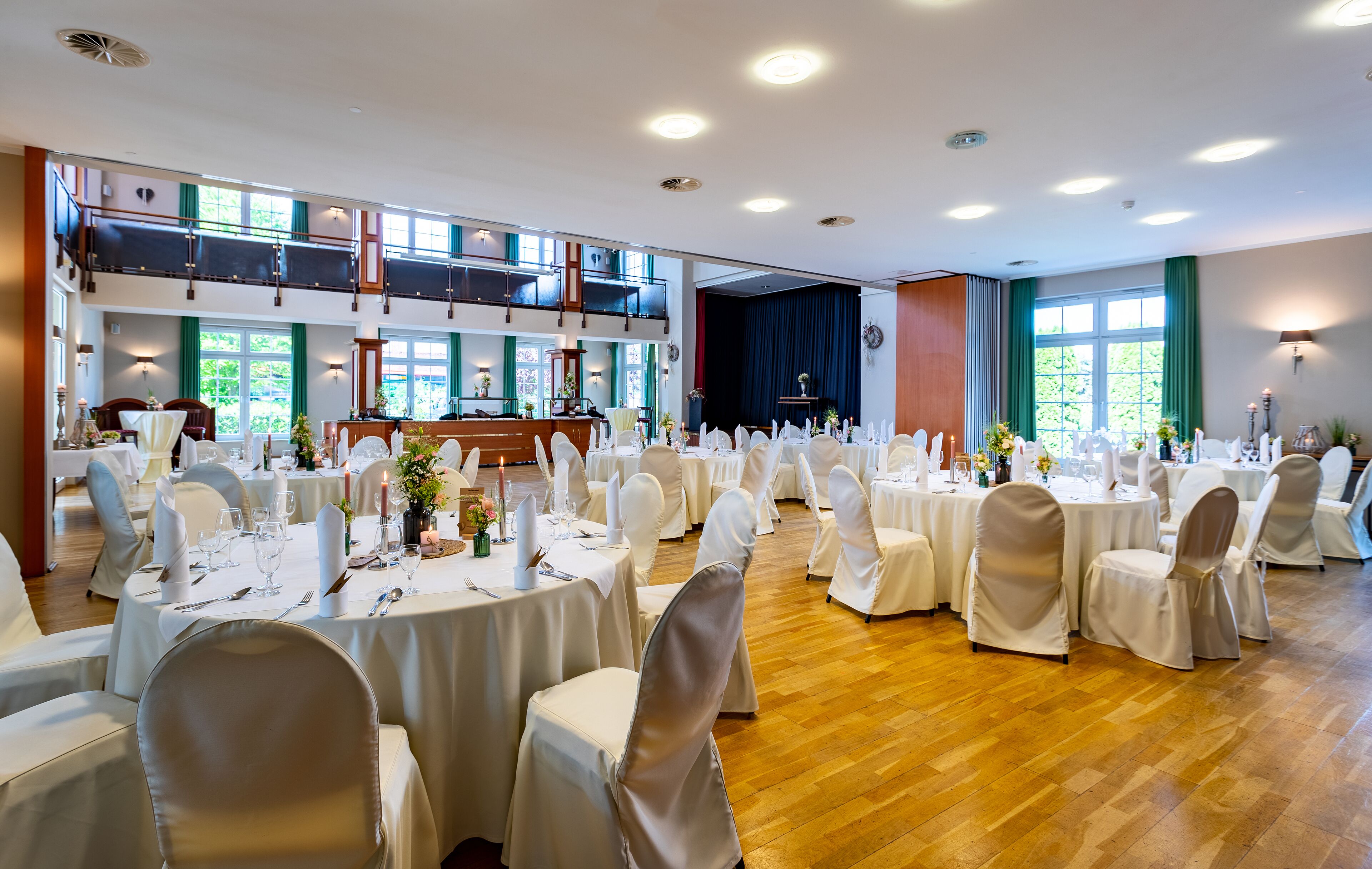 Une salle de banquet avec des tables rondes, des chaises blanches et un plafond haut orné de nombreux luminaires.