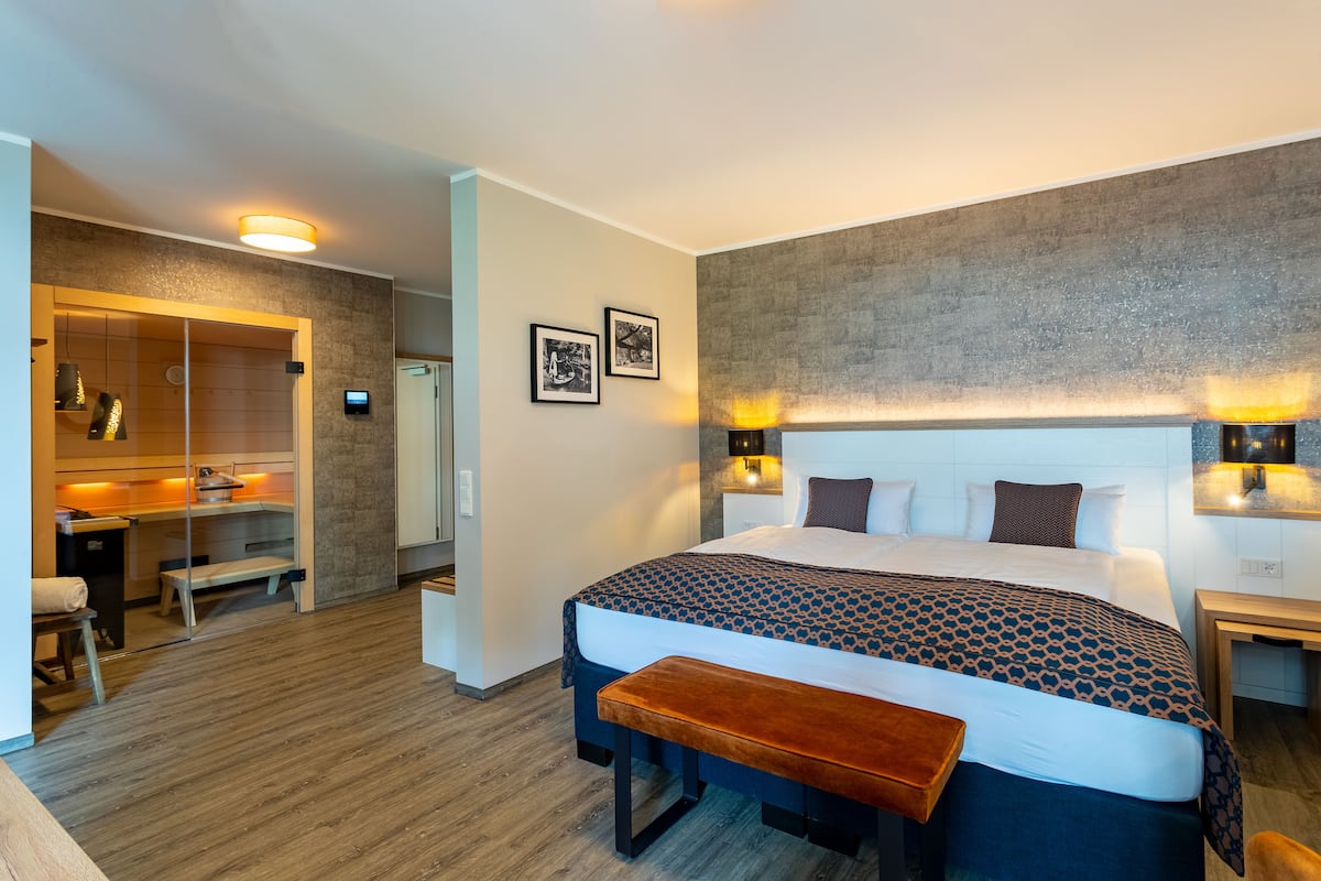 Une chambre d’hôtel moderne équipée d’un grand lit, de tables de chevet, d’une banquette, d’un bureau et d’une armoire.
