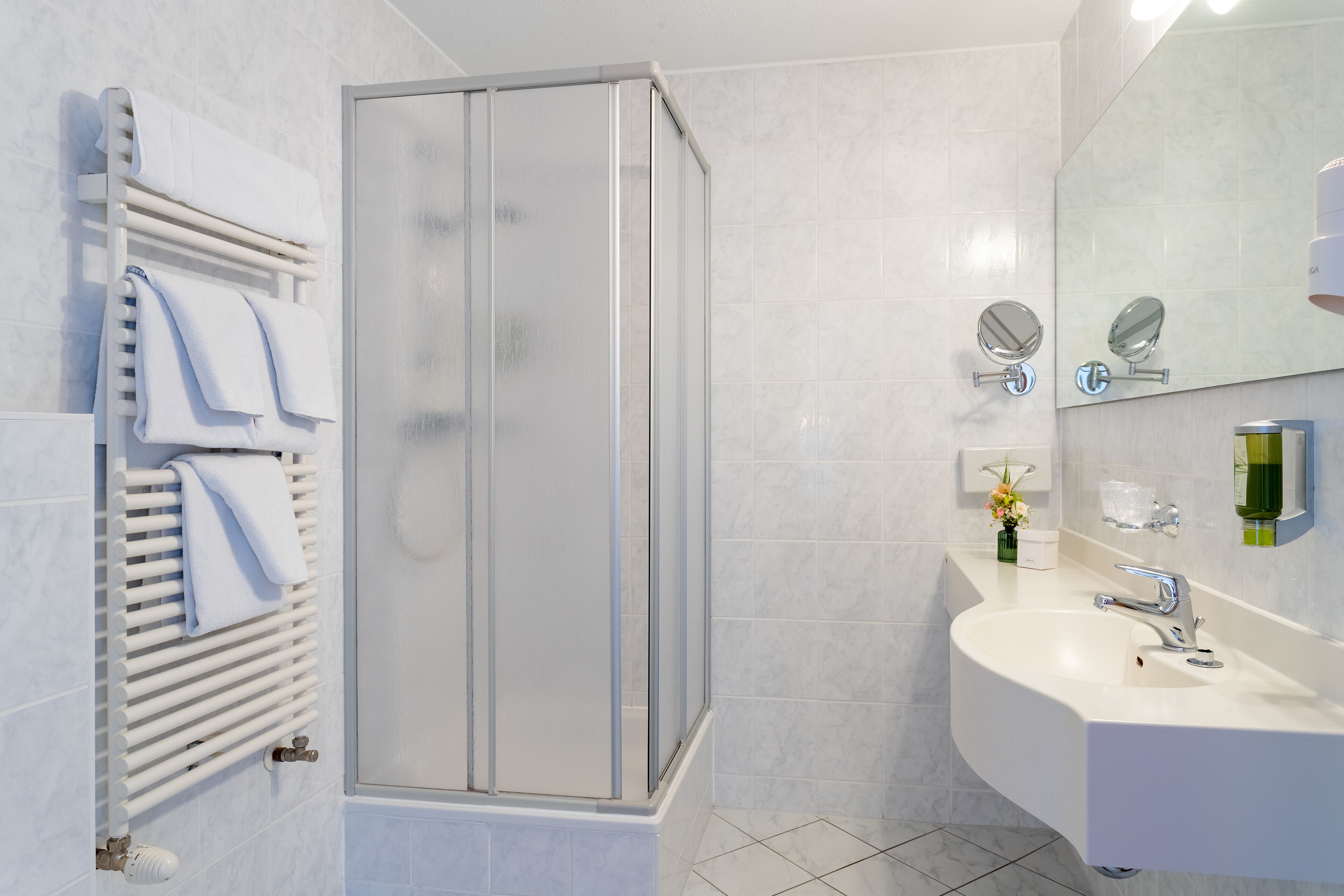 Un baño moderno con cabina de ducha de vidrio, un lavabo blanco con espejo y un perchero con toallas dobladas.