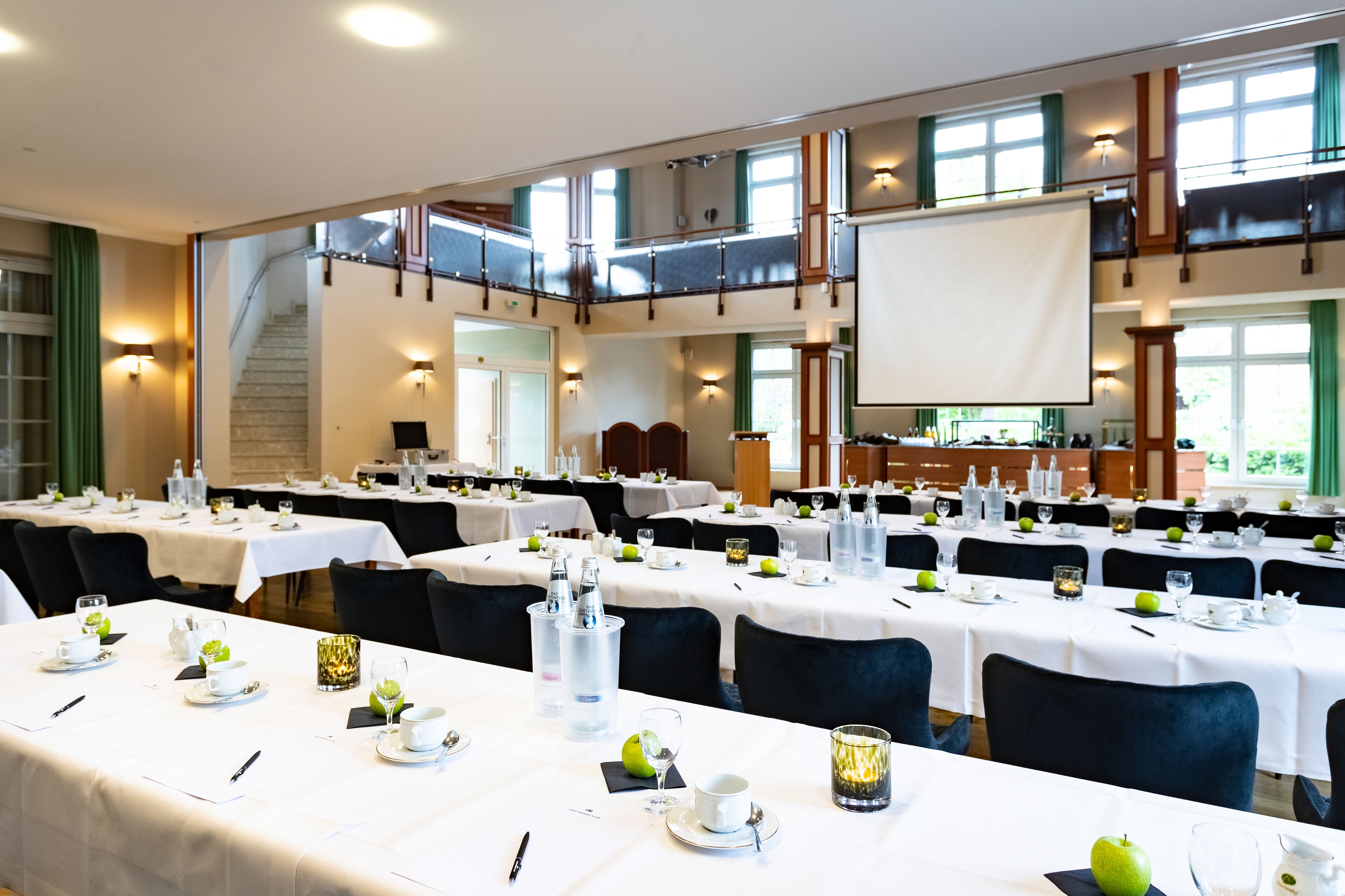 Ein Konferenzraum mit mehreren Tischen, die für eine Besprechung gedeckt sind, mit Namensschildern, Gläsern und einer Projektionsleinwand.