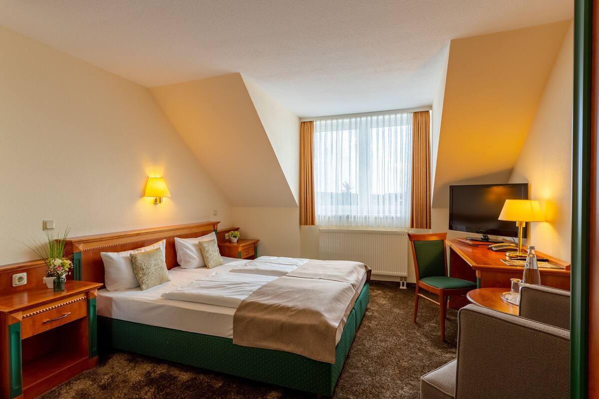 Une chambre d’hôtel avec un grand lit, un bureau avec une chaise, une télévision et une fenêtre avec des rideaux.