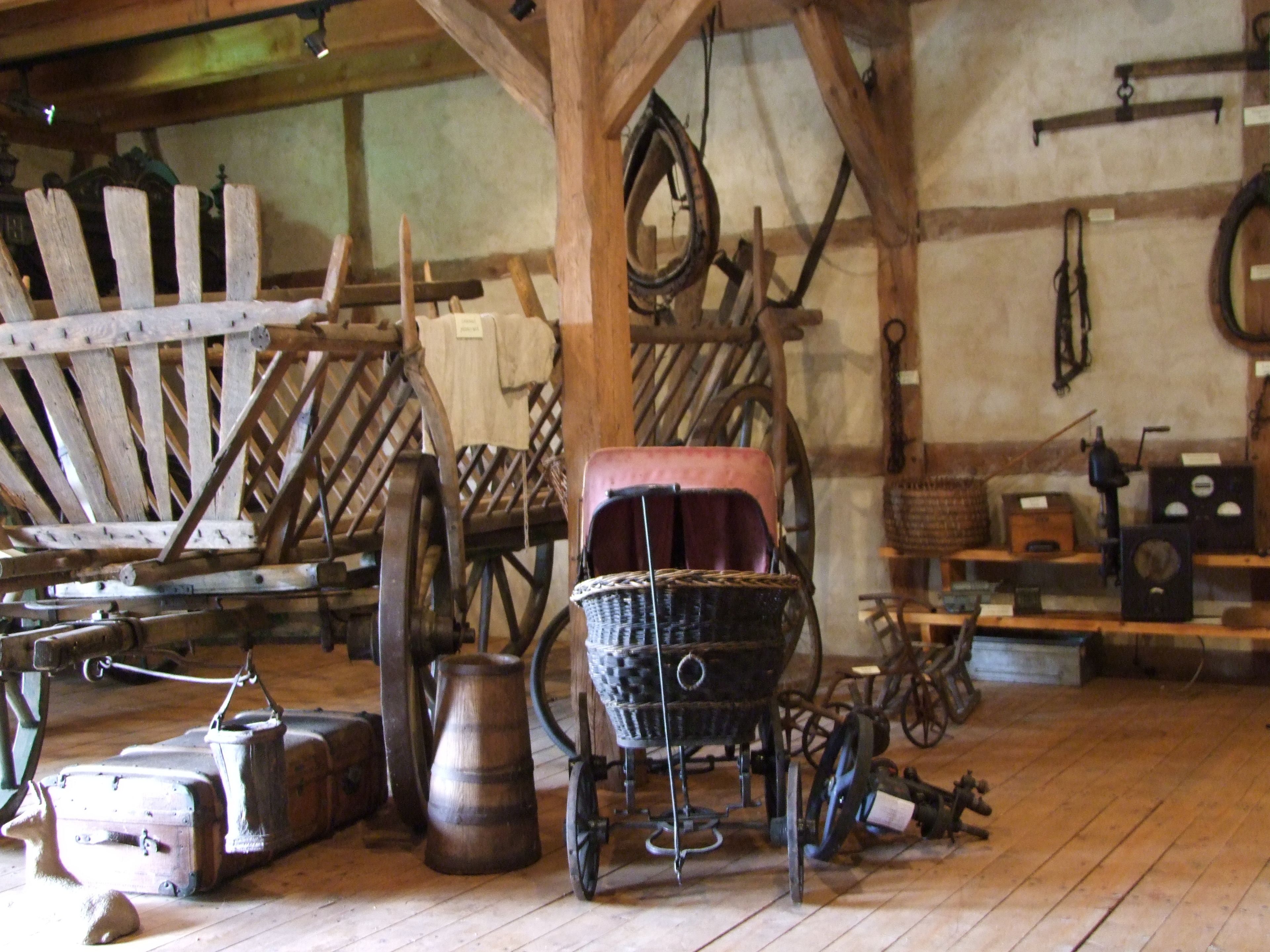 A rustic room with wooden beams, a wooden chair, a wheelbarrow, and various antique items.