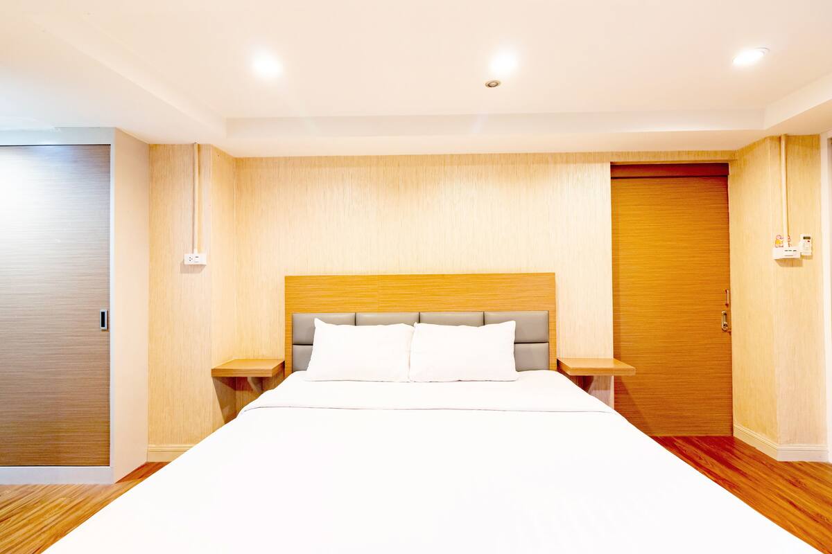 A modern hotel room with a large bed, wooden panel walls, and a wooden door.