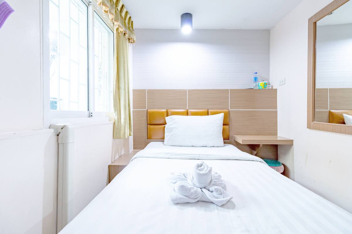 A hotel room with a bed, a bedside table, a mirror, and a window with curtains.