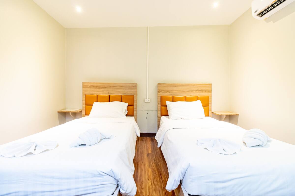 A hotel room with two single beds, wooden headboards, white bedding, and a wooden floor.