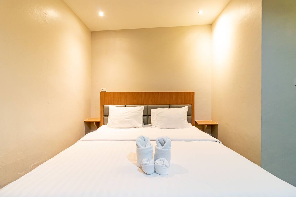 A hotel room with a large bed, two pillows, a wooden headboard, and a pair of towels on the bed.