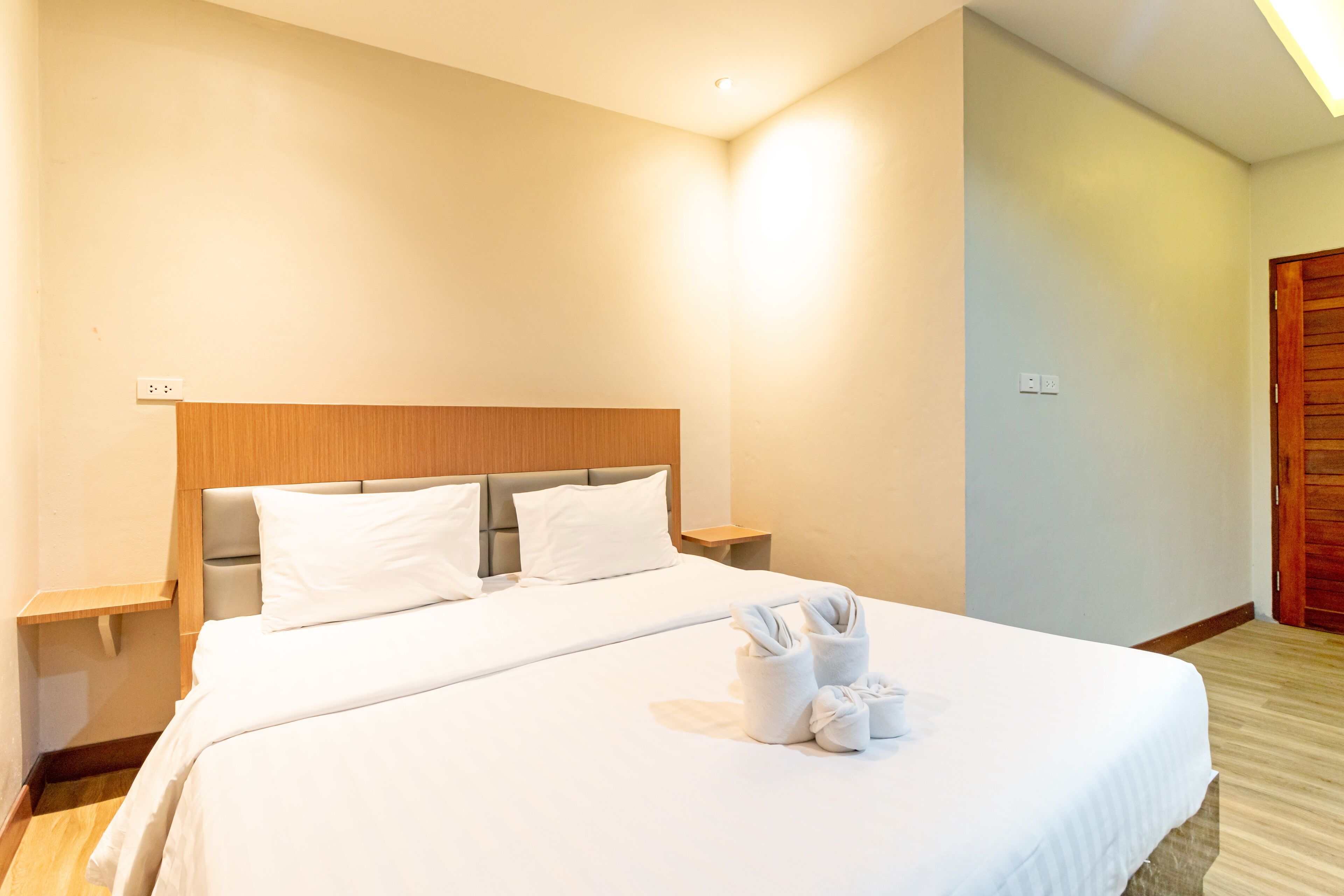 A neatly made bed with white linens and towels, a wooden headboard, and a nightstand with a lamp.